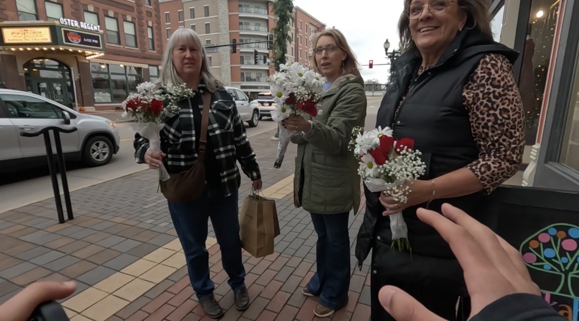 Three women holding bouquets of flowers on a sidewalk