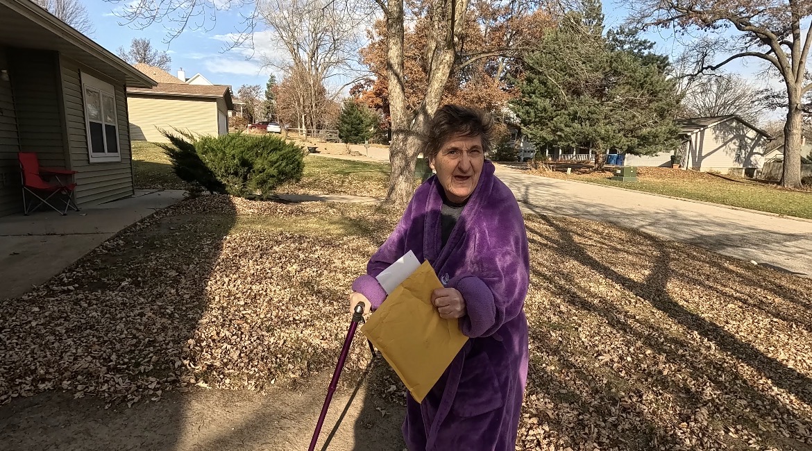 A woman in a purple robe holding a yellow envelope outdoors